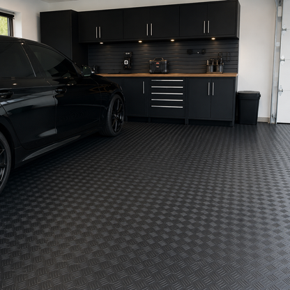 Black 1.5m wide 3mm 5 bar rubber flooring installed in a clean modern UK garage with parked black car and tool cabinets visible