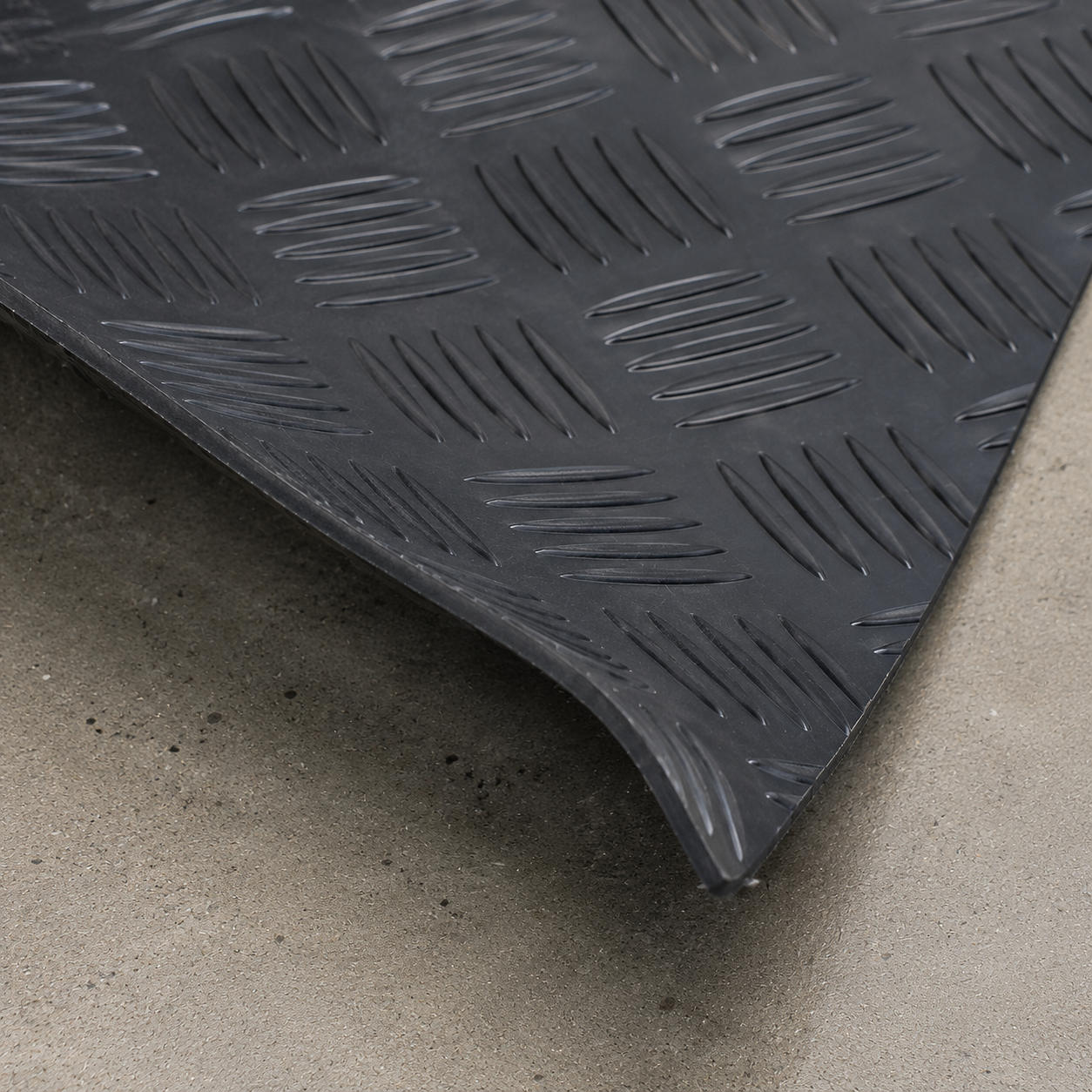 Close-up of black 1.5m wide 3mm 5 bar checker rubber garage flooring, corner slightly lifted to show thickness and flexibility