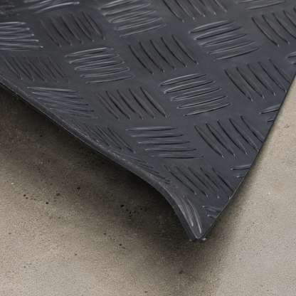 Close-up of black 1.5m wide 3mm 5 bar checker rubber garage flooring, corner slightly lifted to show thickness and flexibility