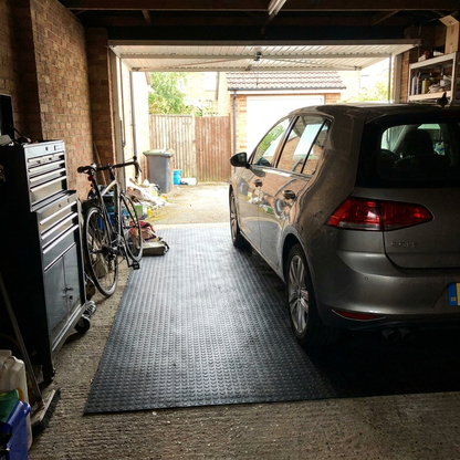 Black coin rubber garage flooring laid in a UK home garage with a car parked on it
