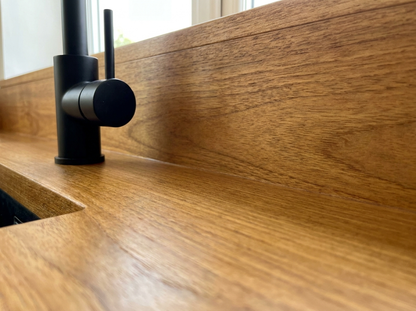 Solid iroko worktop and matching upstand behind a black tap