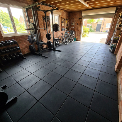 Rubber gym floor tiles in a home garage gym, straight-seam grid, with rack and weights