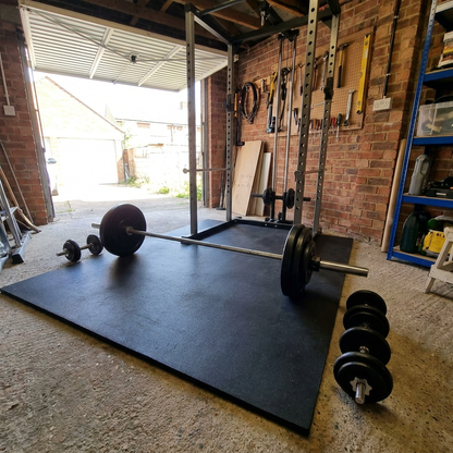 Large rubber gym mat drop pad under a squat rack in a garage gym